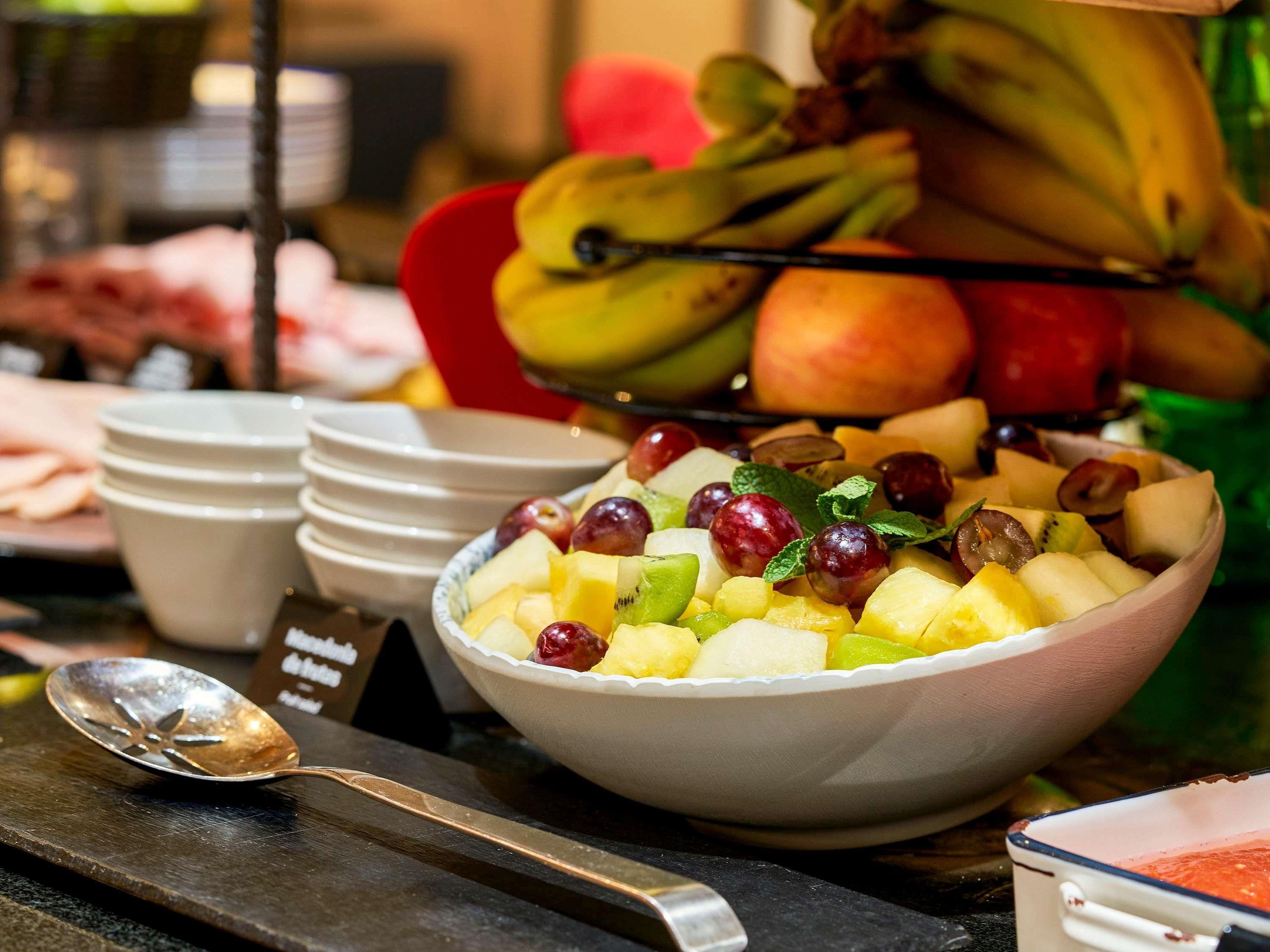 Un frutero con varias frutas y una cuchara sobre una mesa.