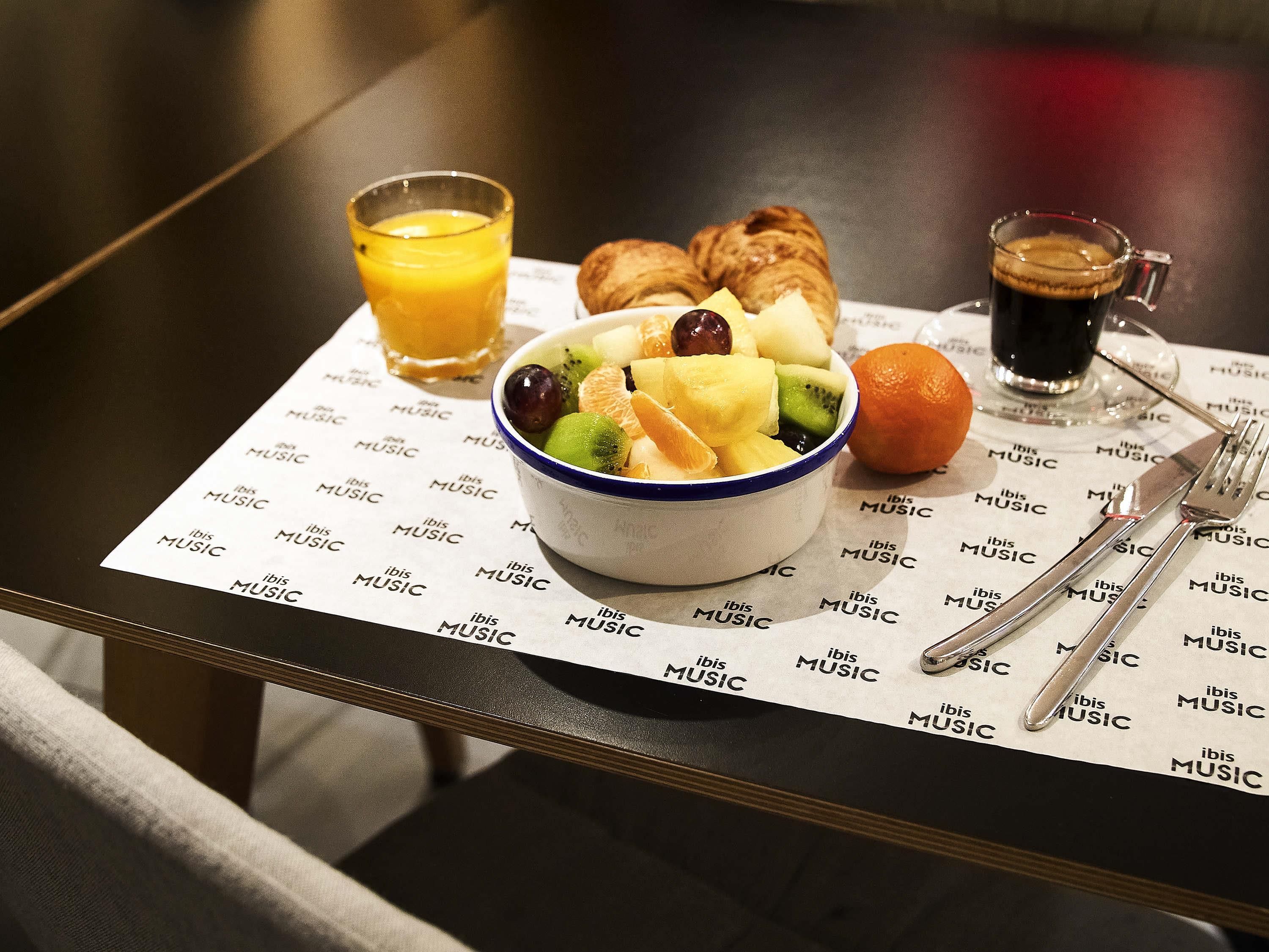 A breakfast setting with a bowl of fruit, orange juice, croissants, and coffee on a table with a music-themed placemat.