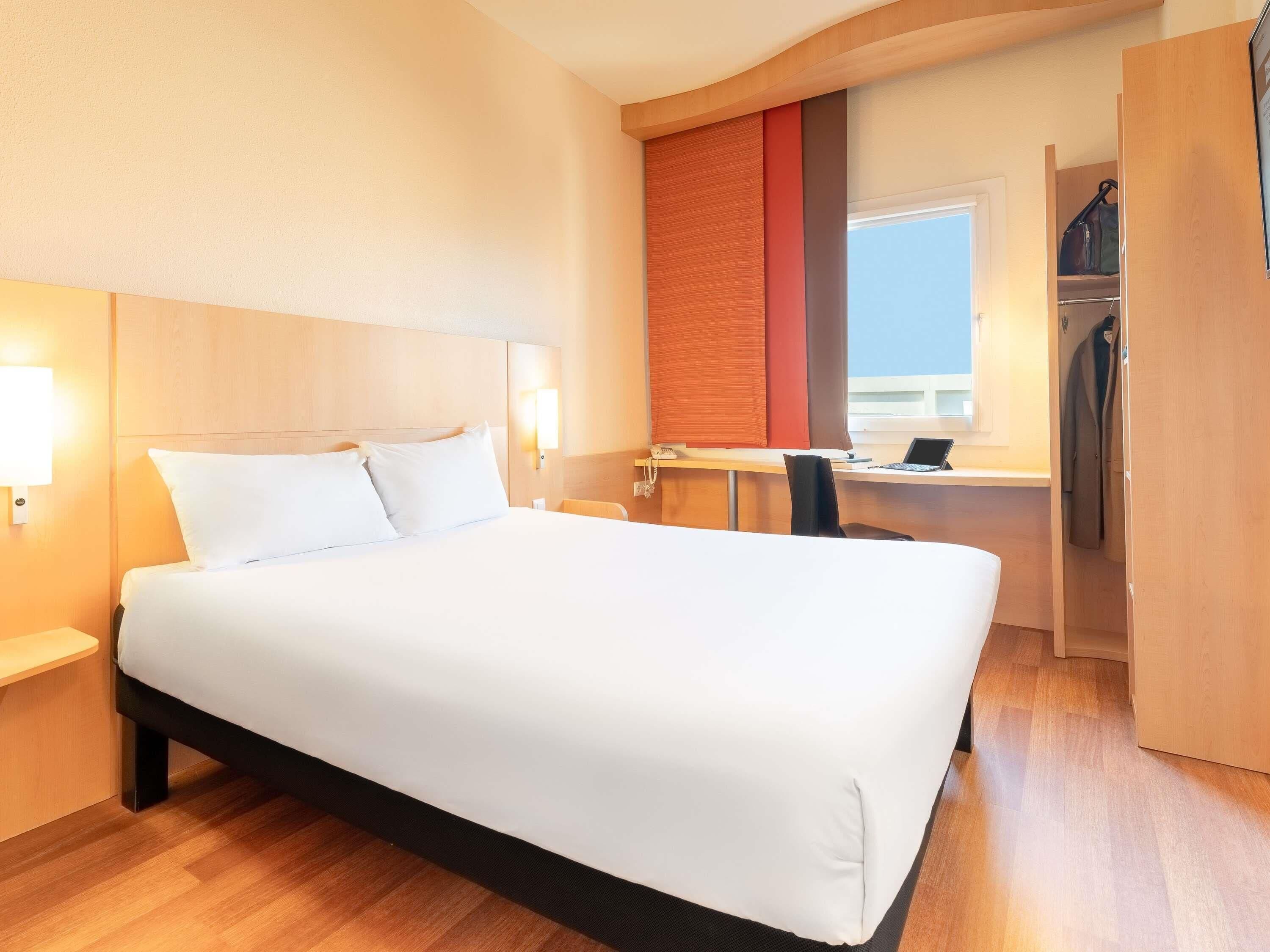 Una habitación de hotel con una cama grande, un escritorio con una computadora, una silla y un armario.