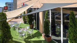 A hotel with outdoor seating, a shaded area, and a view of the parking garage. - ibis Madrid Calle Alcala (Madrid)