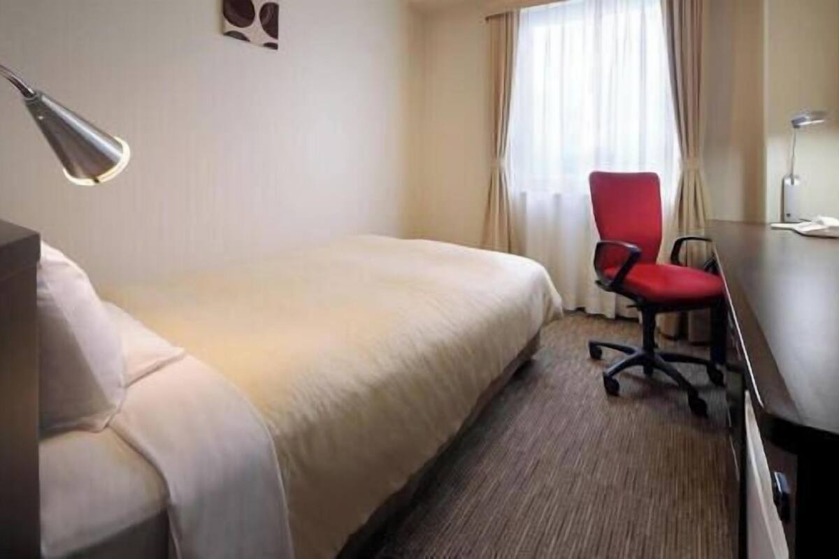 Une chambre d’hôtel avec un lit, un bureau et une chaise, une télévision et une fenêtre avec des rideaux.