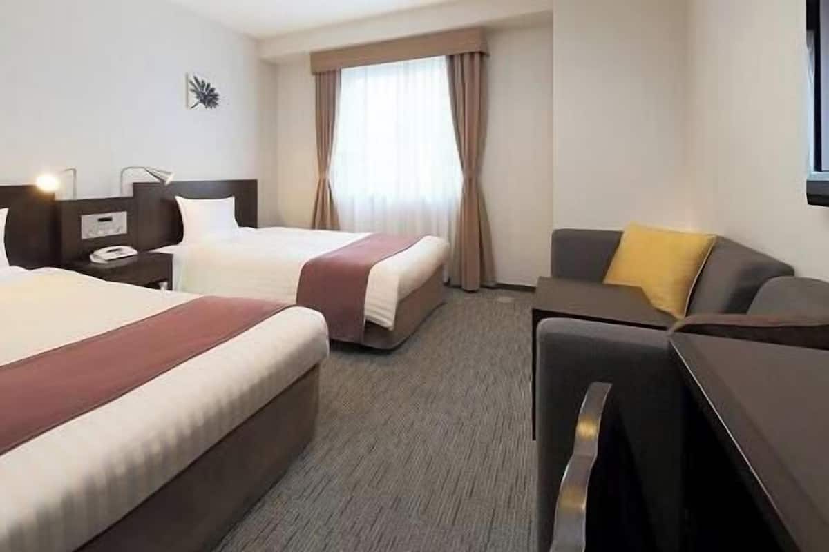 Une chambre d’hôtel avec deux lits, un bureau, une chaise et une fenêtre avec des rideaux.