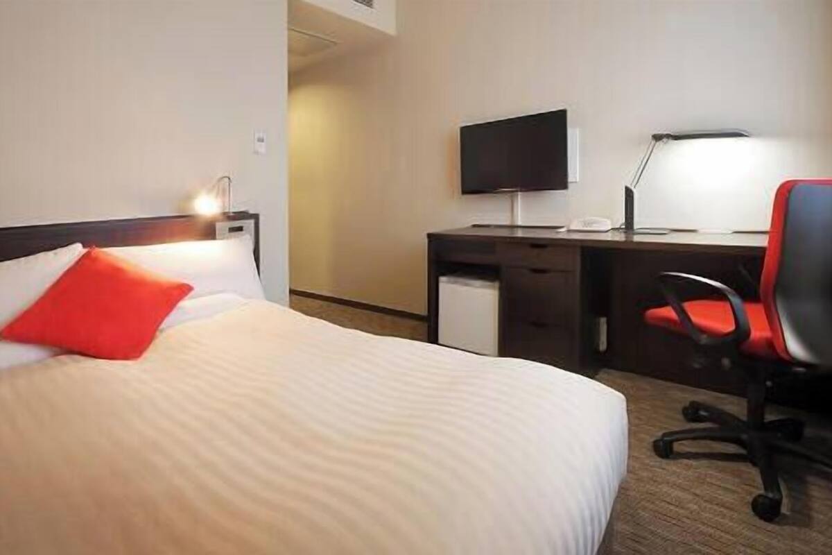 Une chambre d’hôtel avec un lit, un bureau, une chaise, une télévision et une lampe.