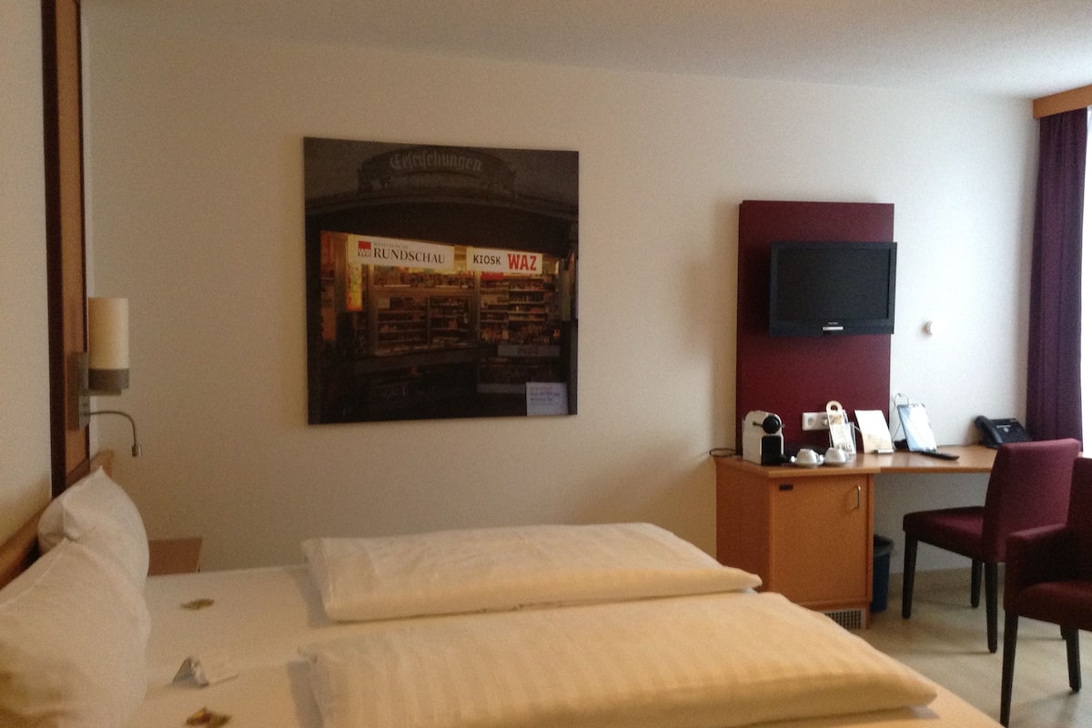 A hotel room with two beds, a desk with a chair, a television, and a poster on the wall.