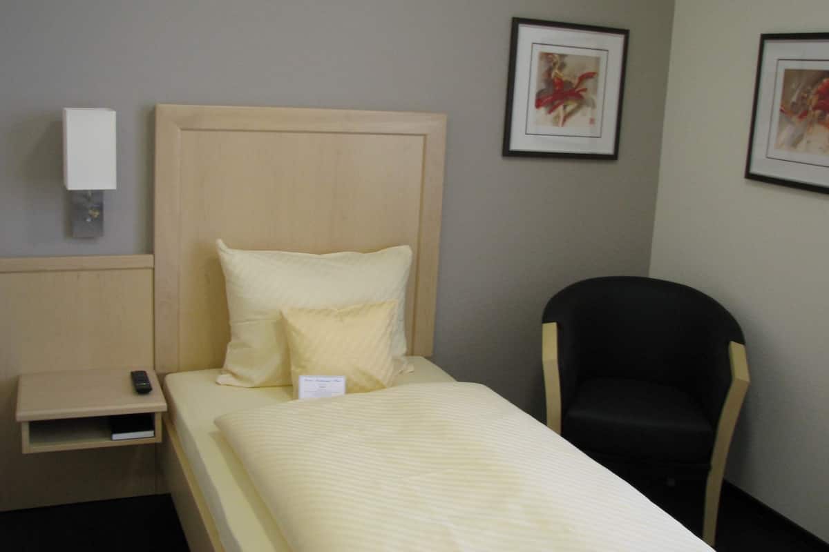 A single bed with a wooden headboard, a bedside table with a remote control, and two framed pictures on the wall.