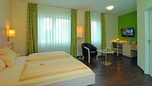 Ett hotellrum med en stor säng, ett skrivbord med en stol, en tv och ett litet bord.