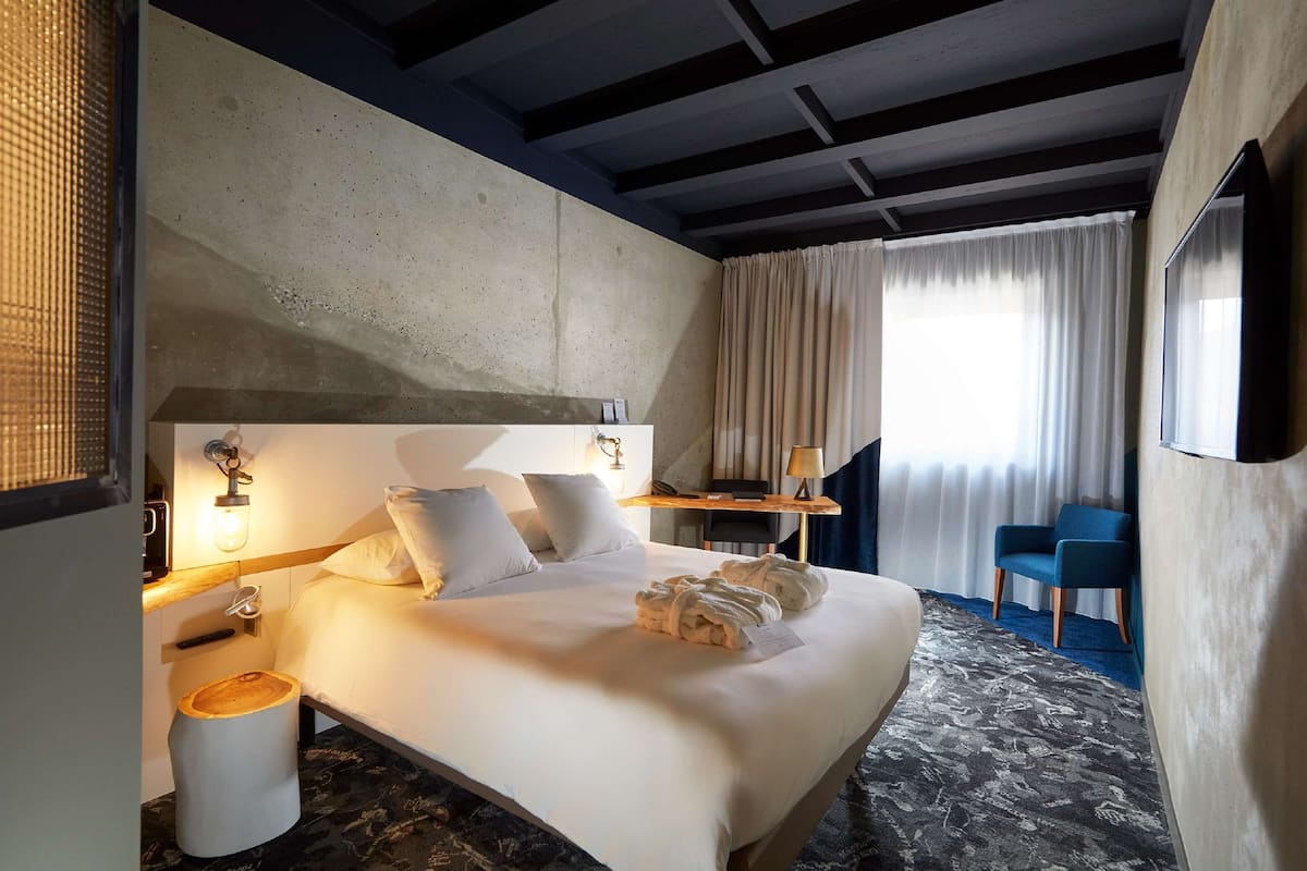 Habitación de hotel con una cama grande, un escritorio, una silla y vistas al exterior.