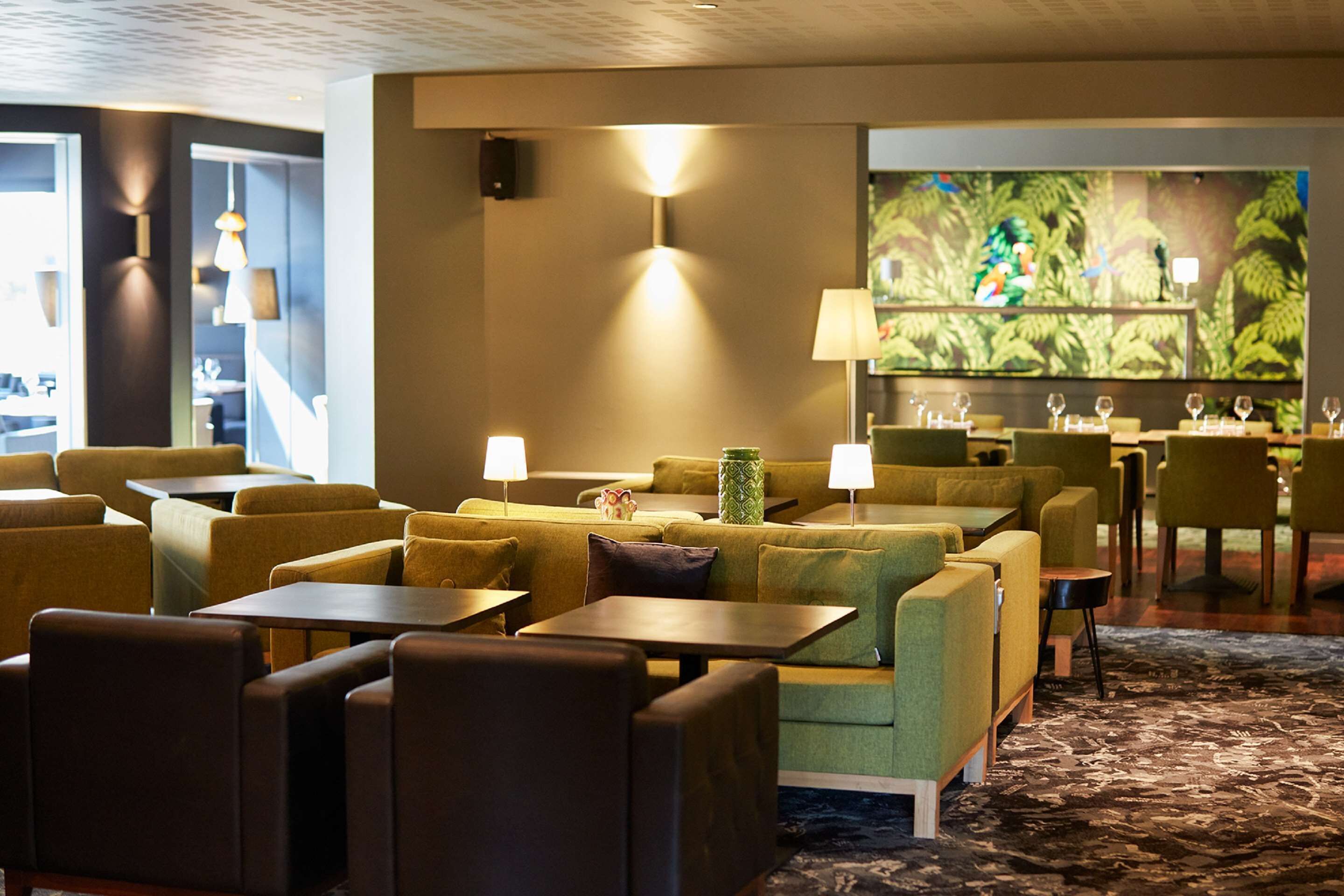 A hotel lobby with green sofas, tables, and a large screen displaying a nature scene.