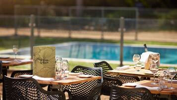 Un área de comedor al aire libre con mesas y sillas, un menú y una piscina al fondo.