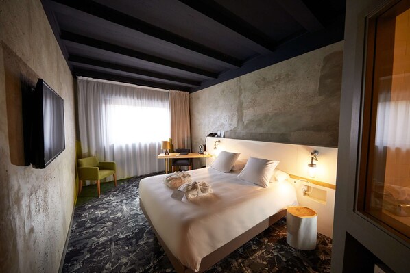Una habitación de hotel con una cama grande, un televisor de pantalla plana montado en la pared, un escritorio con una silla y una ventana con cortinas.