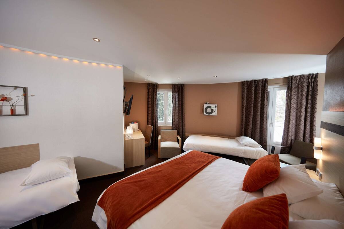 Habitación de hotel con dos camas individuales, un escritorio con silla, una ventana con cortinas y un aire acondicionado instalado en la pared.