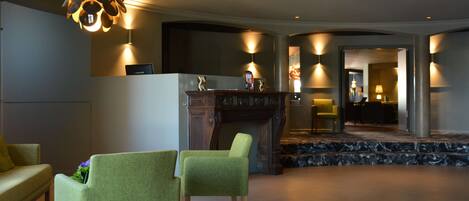A lobby with a reception desk, two green chairs, a decorative light fixture, and a marble staircase.