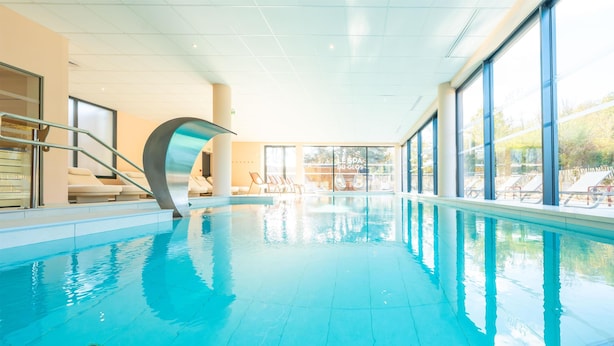 An indoor swimming pool with clear blue water, a curved glass wall, and a view of the outside.