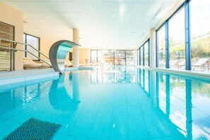 An indoor swimming pool with clear blue water, a curved glass wall, and a view of the outside. - Best Western Premier Clos Syrah Hotel & Spa (Valence)