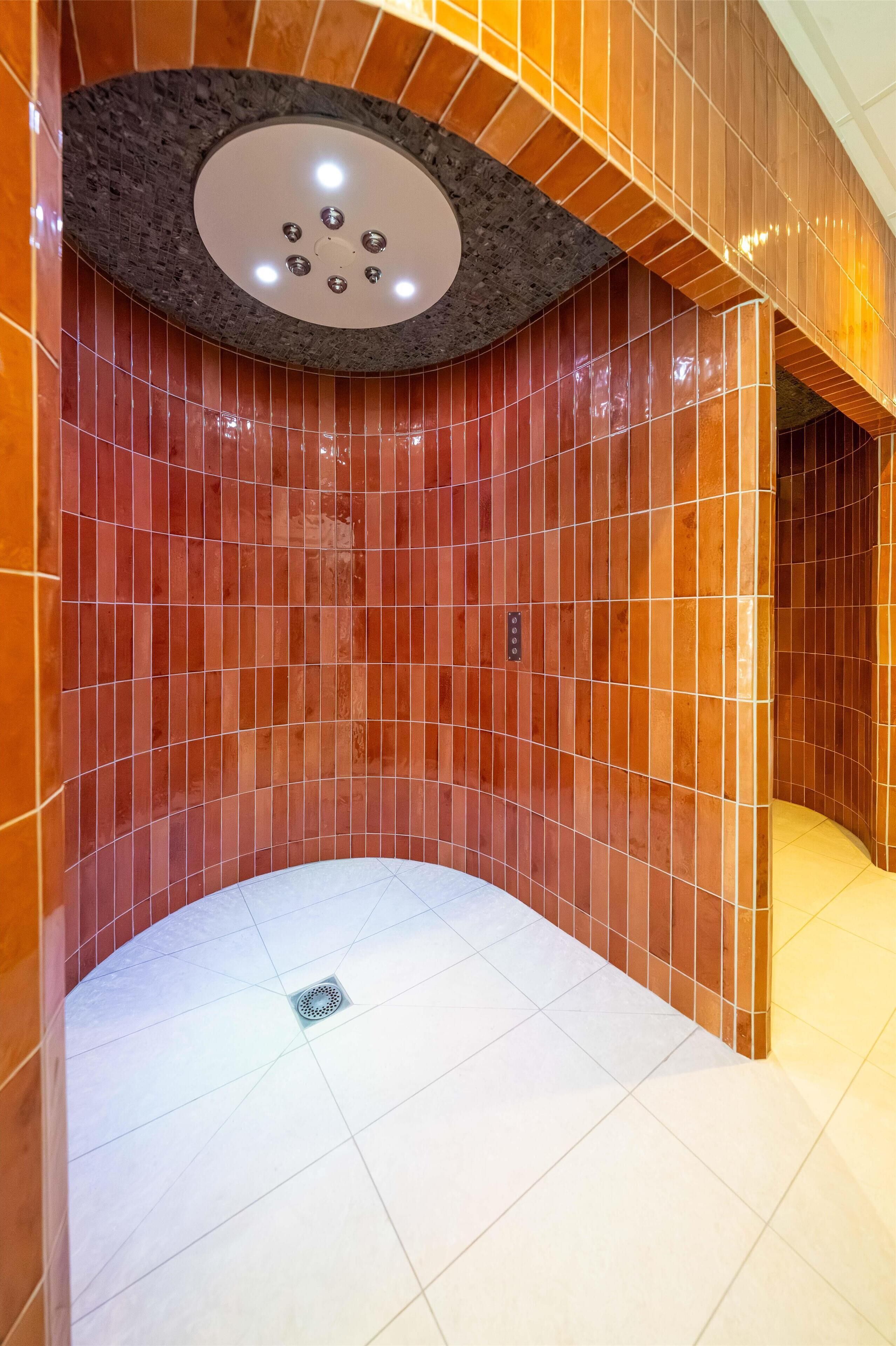 A modern bathroom with a curved design, featuring a combination of red and white tiles, a central light fixture, and a drain in the floor.