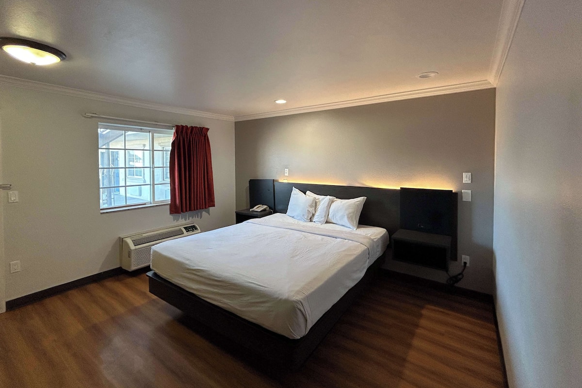 Une chambre d’hôtel avec un grand lit, une table de chevet avec un téléphone, une fenêtre avec des rideaux et un radiateur fixé au mur.