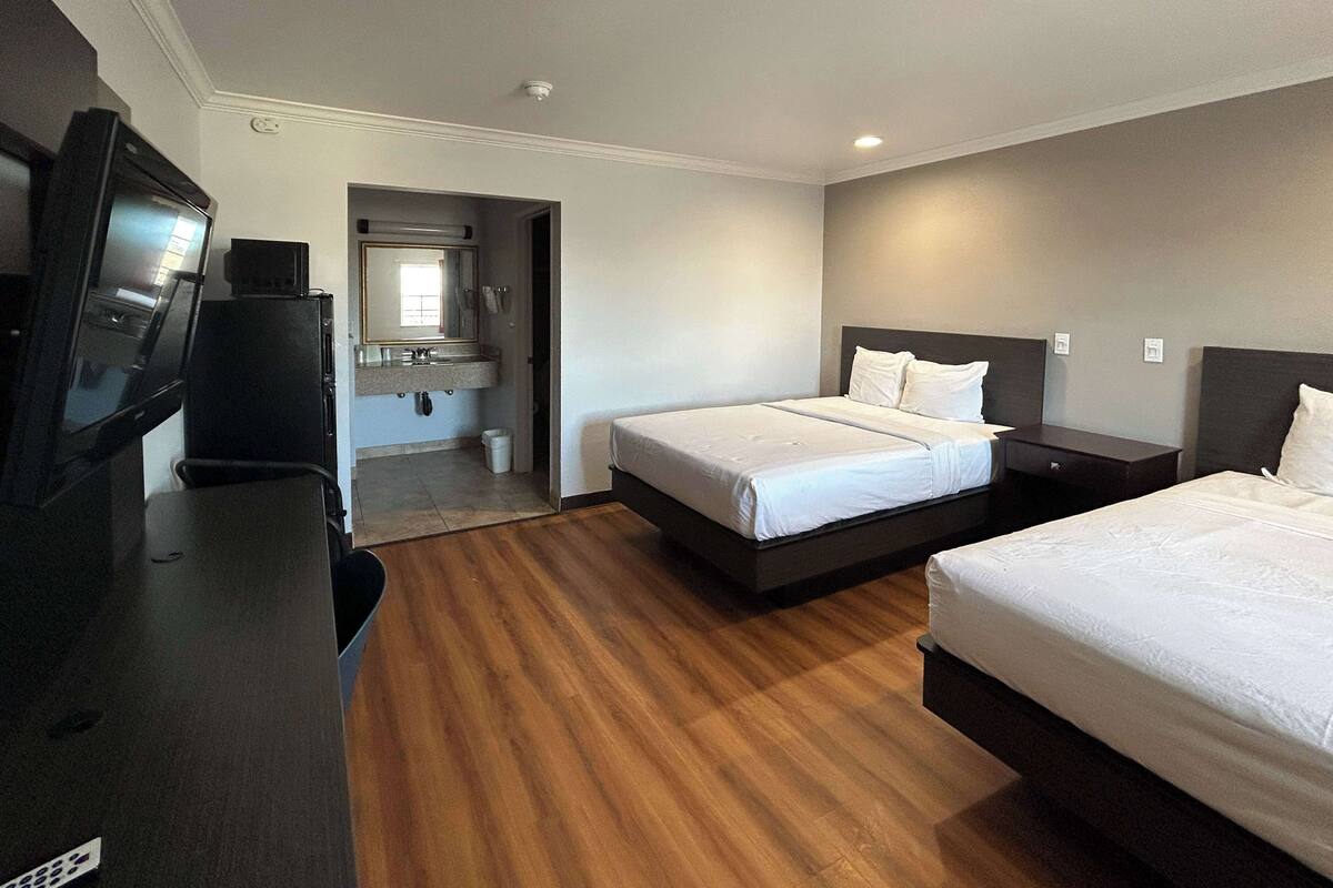 Une chambre d’hôtel avec deux lits, une télévision, un bureau et une salle de bain visible à travers une porte ouverte.