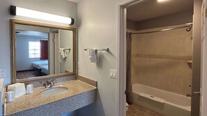 Un bagno con lavabo su piano in granito, uno specchio grande e zona doccia.