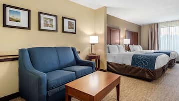 Una habitación de hotel con un sofá azul, una mesa de centro de madera, una cama con dos almohadas y cuadros en la pared.
