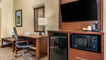 A hotel room with a desk, chair, television, microwave, and coffee maker.