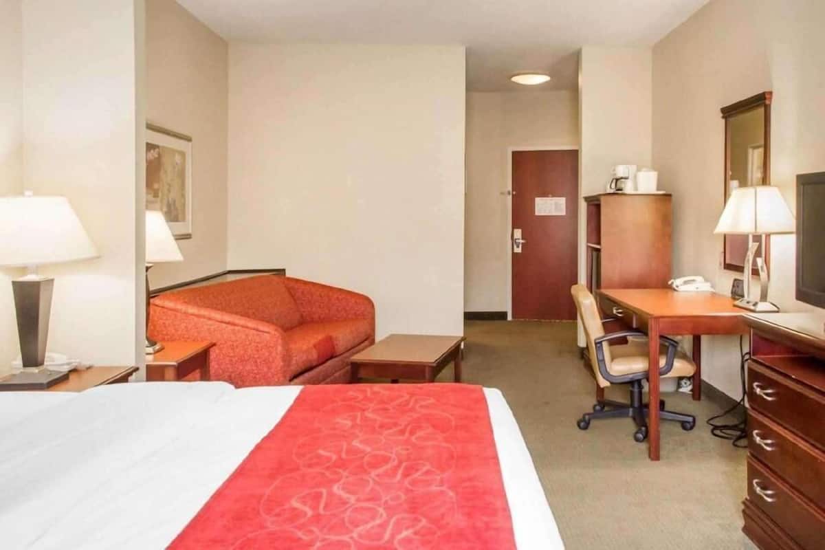 Een hotelkamer met een bed, bureau, stoel, lamp en een kledingkast.