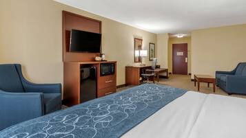 A hotel room with a large bed, two armchairs, a desk with a television, microwave, and coffee maker.