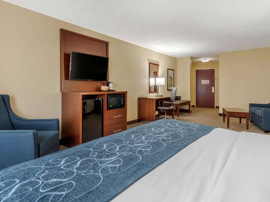 A hotel room with a large bed, two armchairs, a desk with a television, microwave, and coffee maker.