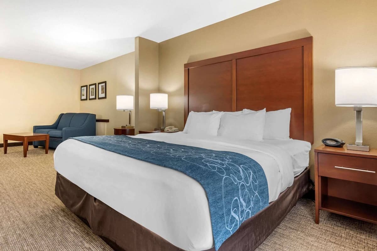 A hotel room with a large bed, a desk, a chair, two bedside lamps, and a clock on the nightstand.