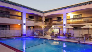 A hotel pool area with a clear pool, outdoor seating, and a staircase leading to the upper floors.