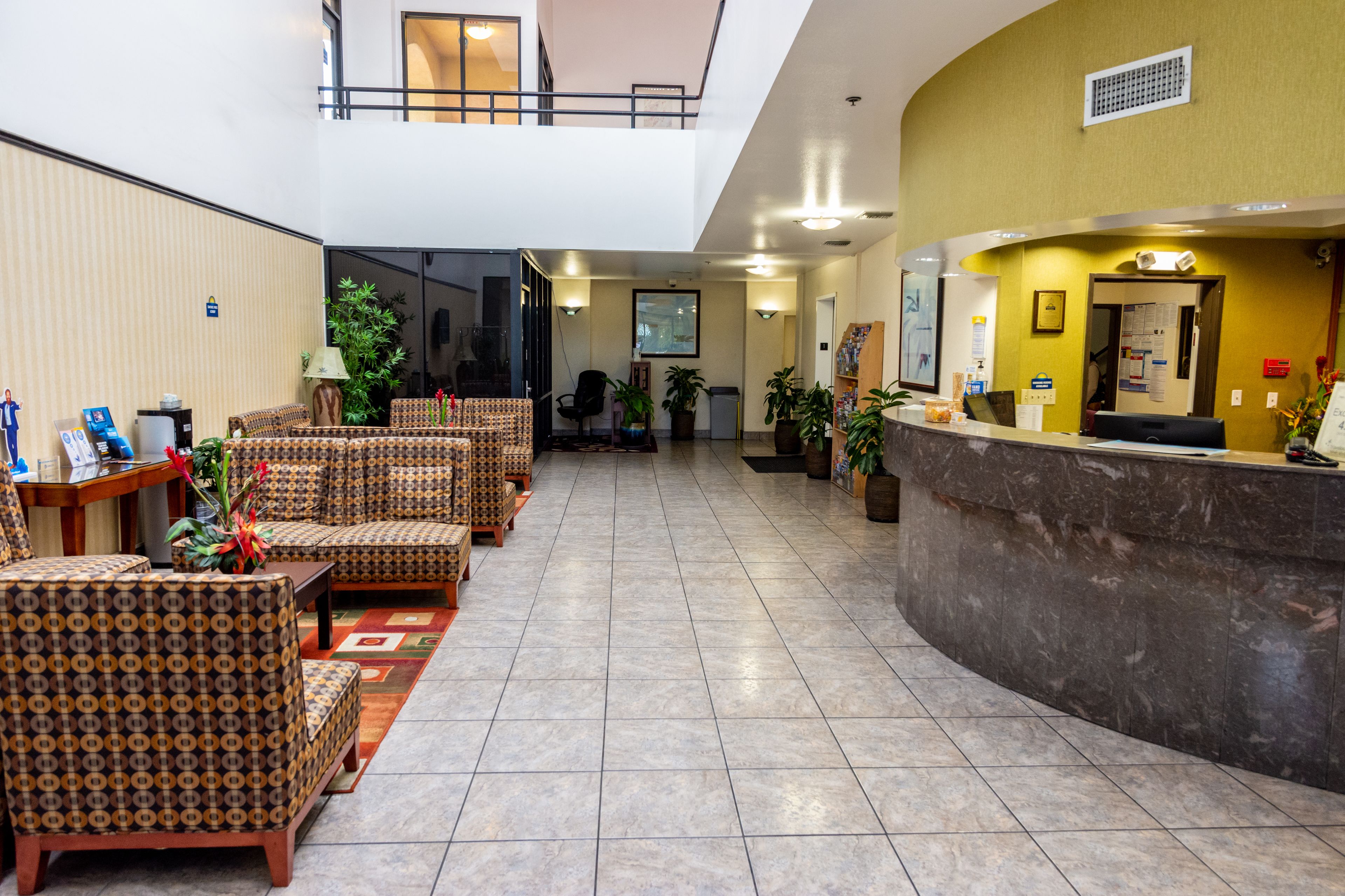 A hotel lobby with a reception desk, seating area, and a staircase leading to an upper level.