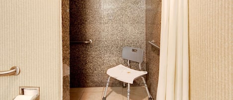 Un baño accesible para sillas de ruedas con pared de granito, dispensador de papel higiénico y cortina de ducha.