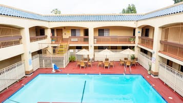 A hotel with a central swimming pool, multiple balconies, and outdoor seating areas.