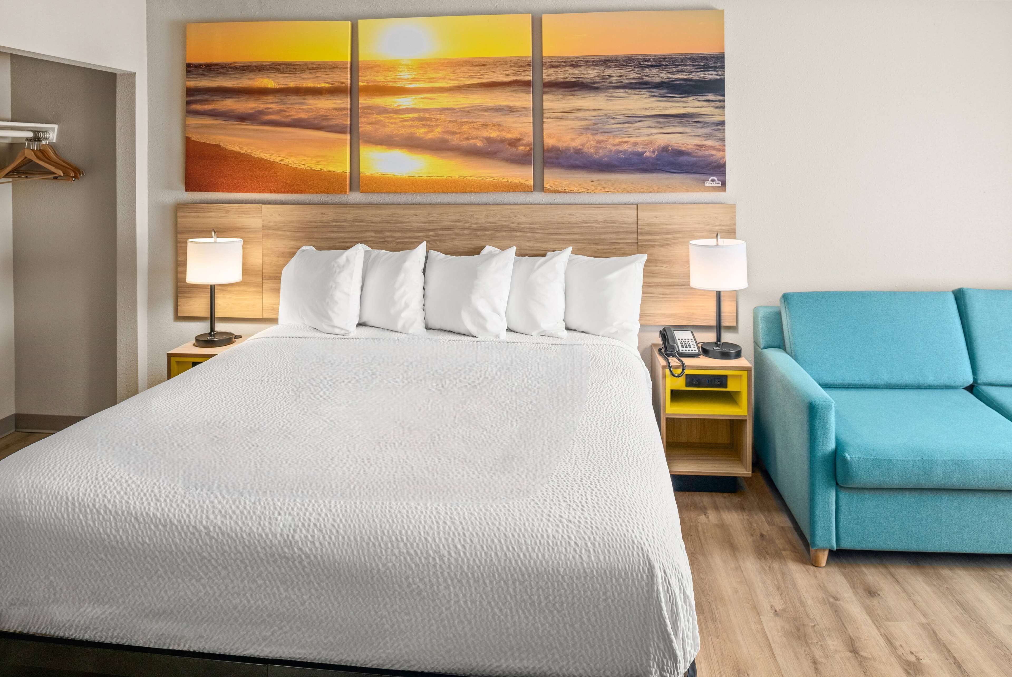 Una cama bien hecha con ropa blanca, un cabecero de madera, lámparas de noche, una mesita de noche de madera y un sillón azul.