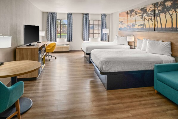 A hotel room with two beds, a desk with a computer, a chair, and a couch. - Days Inn & Suites by Wyndham Artesia (Artesia)