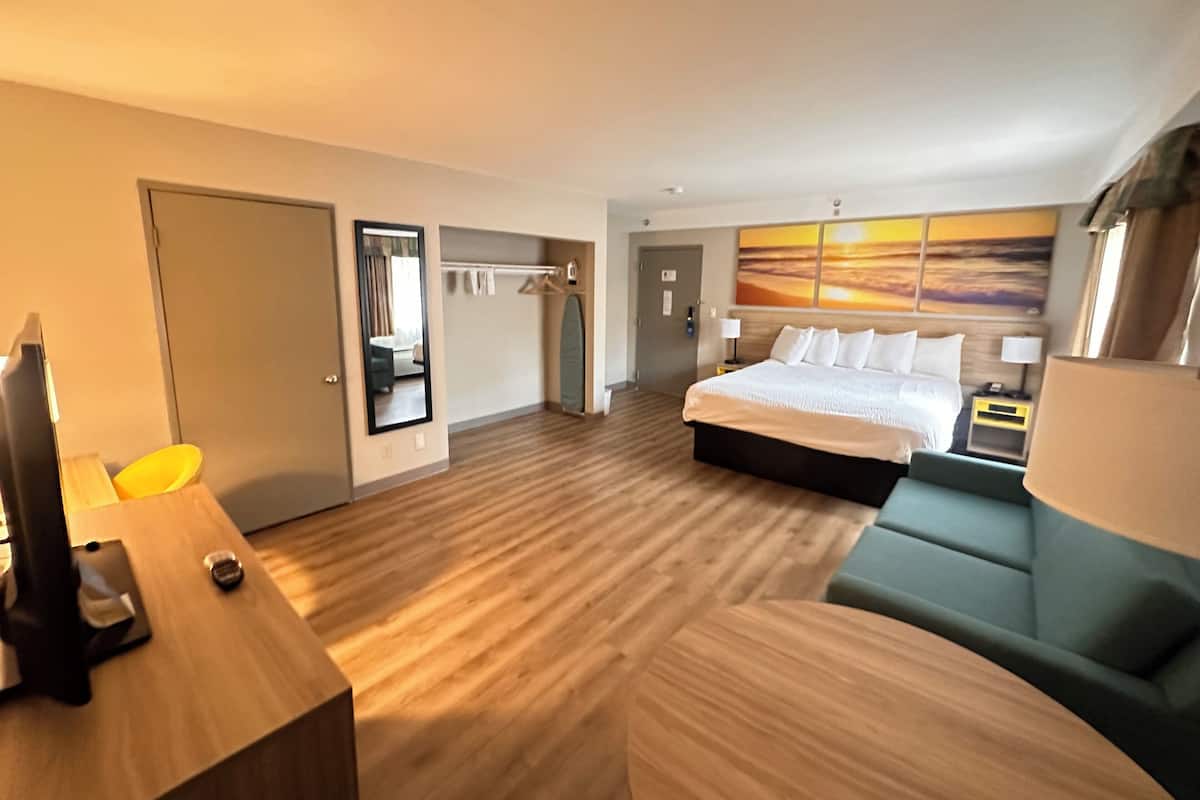 Une chambre d’hôtel avec un lit, un bureau, une chaise, un porte-manteau et un tableau au mur.