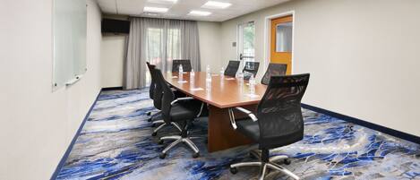 A conference room with a long table, black chairs, and a patterned carpet.