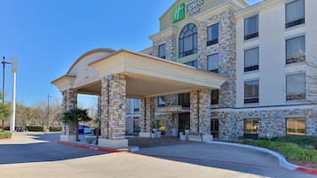 Un bâtiment de l’hôtel Holiday Inn Express & Suites, avec une façade en pierre, une entrée couverte et un ciel d’un bleu éclatant.