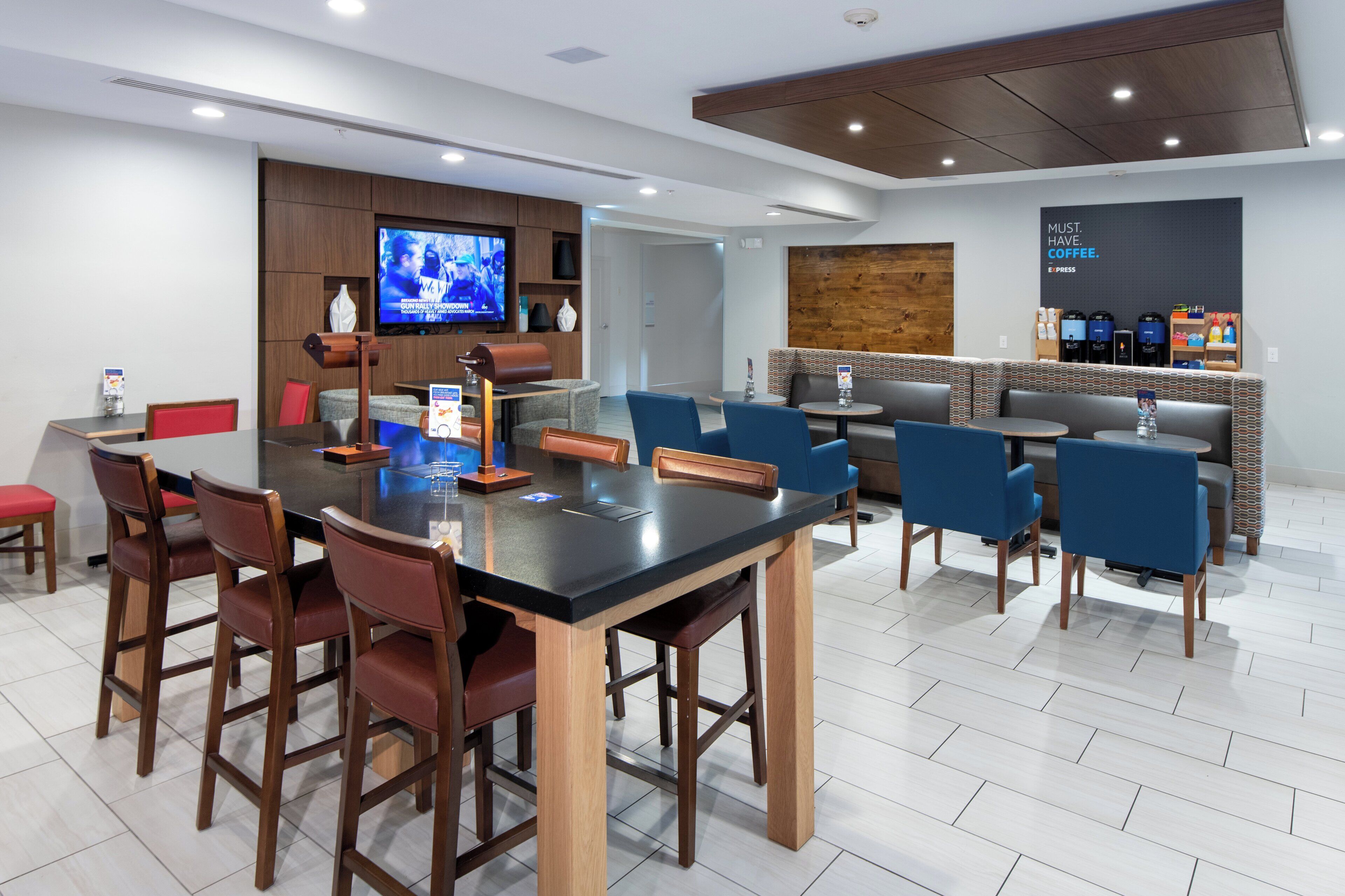 A modern hotel lobby with a central dining area, seating arrangements, and a coffee bar.