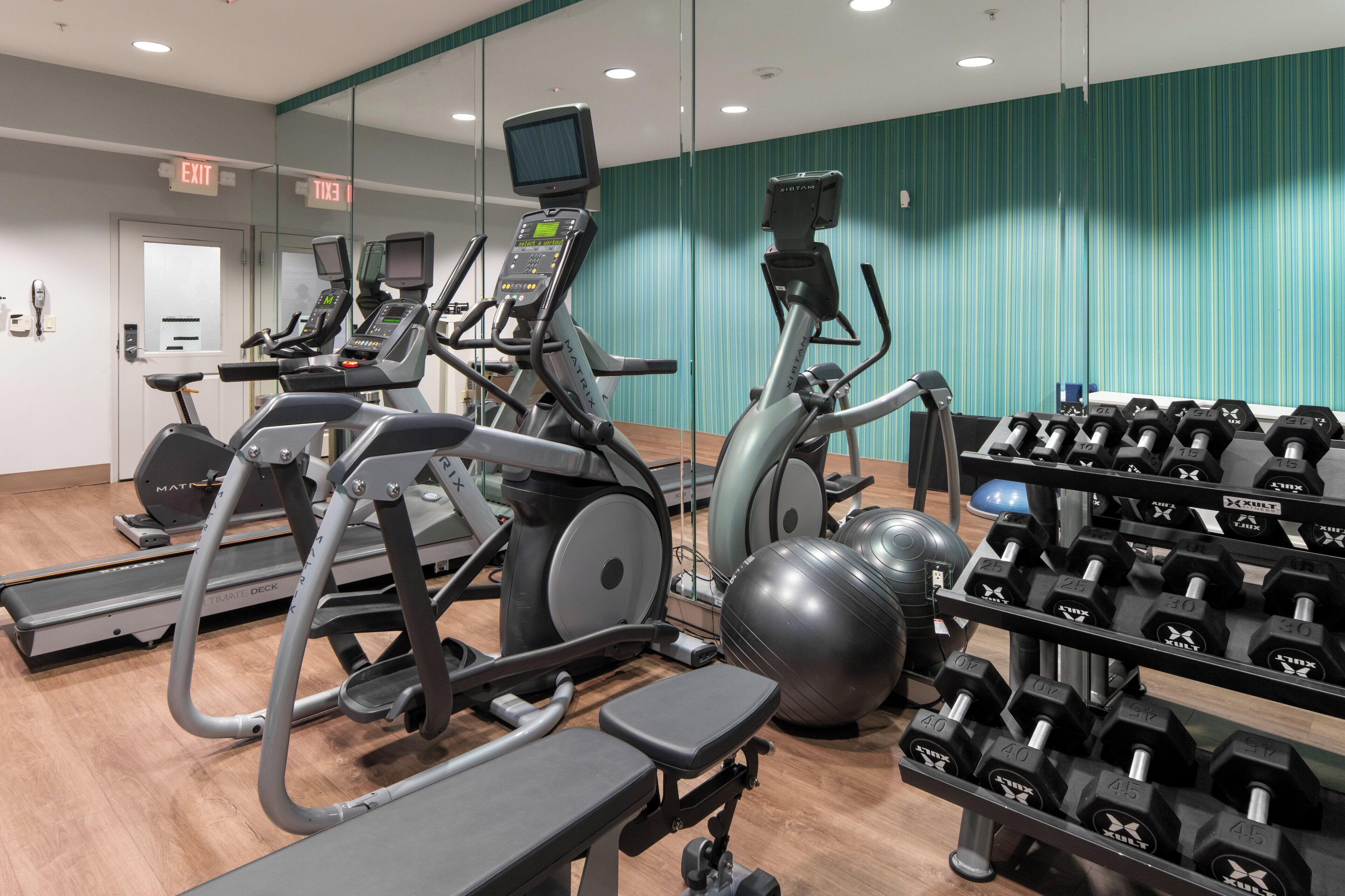 Un gimnasio con cintas de correr, bicicletas estáticas y un soporte para pesas con mancuernas.