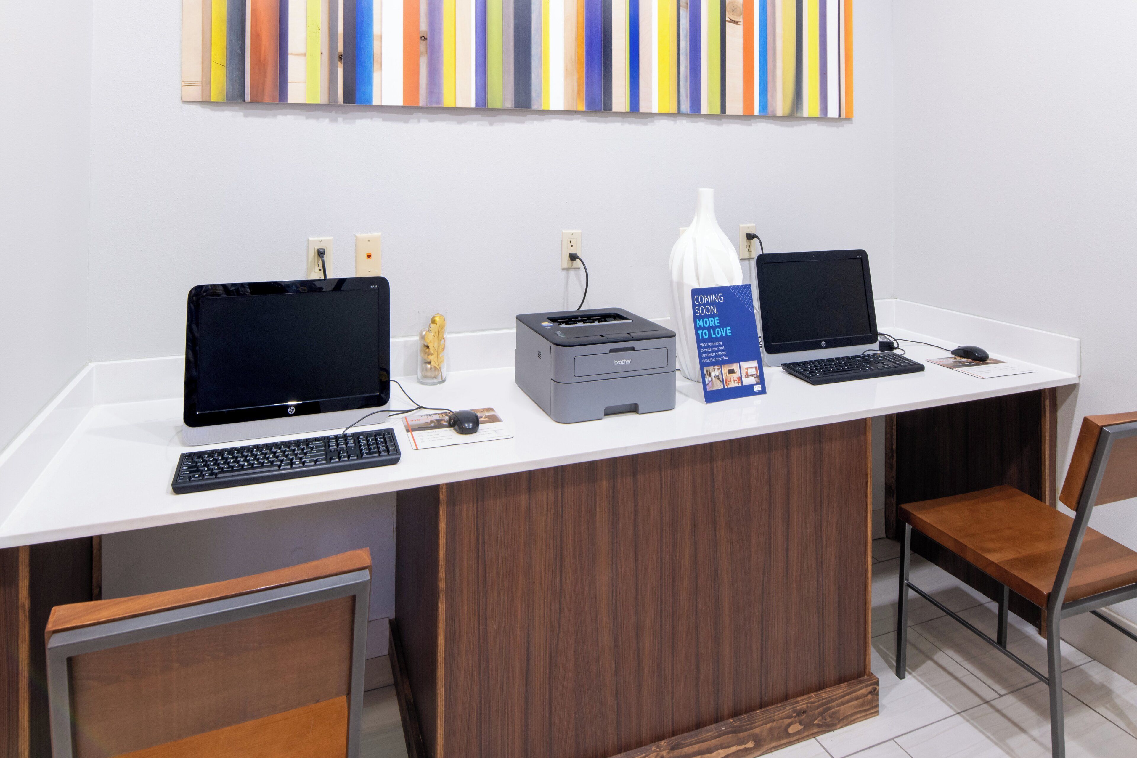 Un comptoir d’accueil avec deux ordinateurs portables HP, une imprimante Brother et un vase.