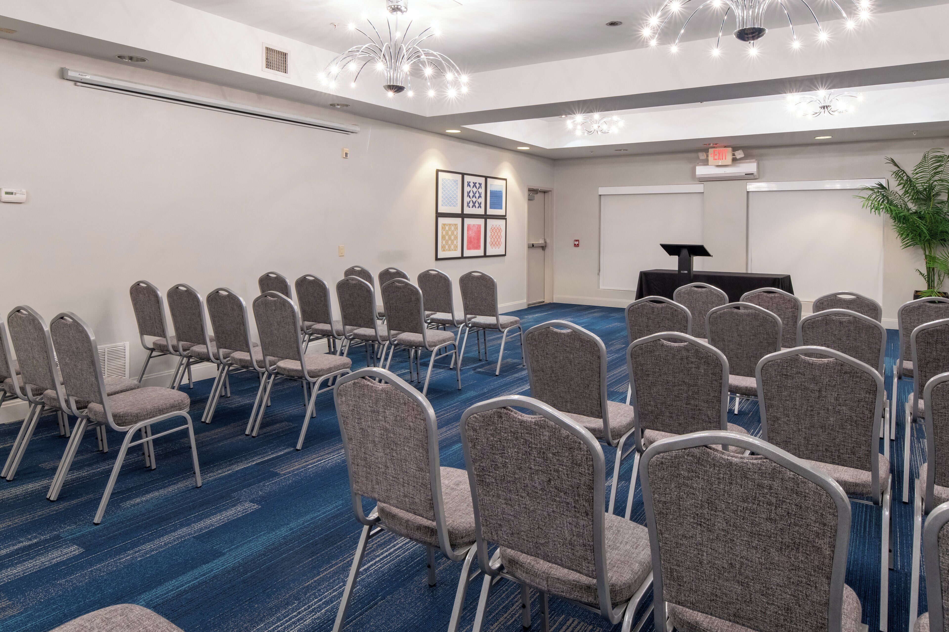 Un salón de conferencias con filas de sillas, un atril y una pantalla para proyector.