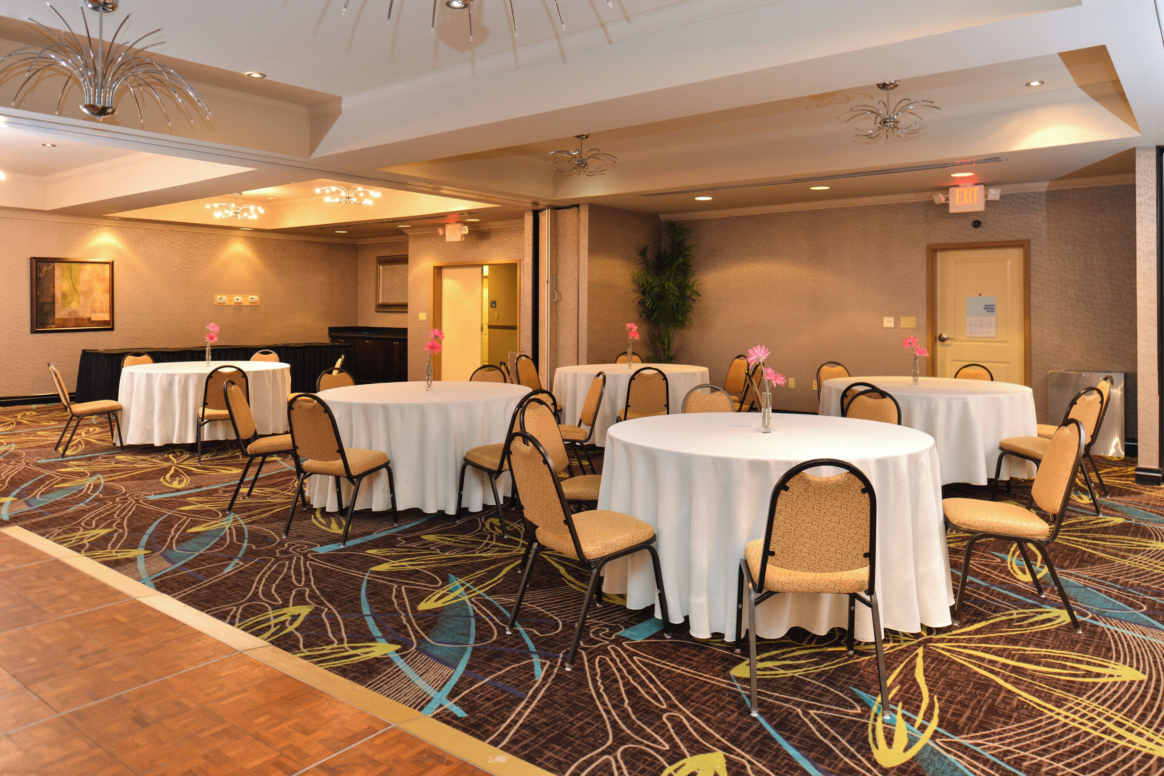 A conference room with round tables, chairs, and a carpeted floor.