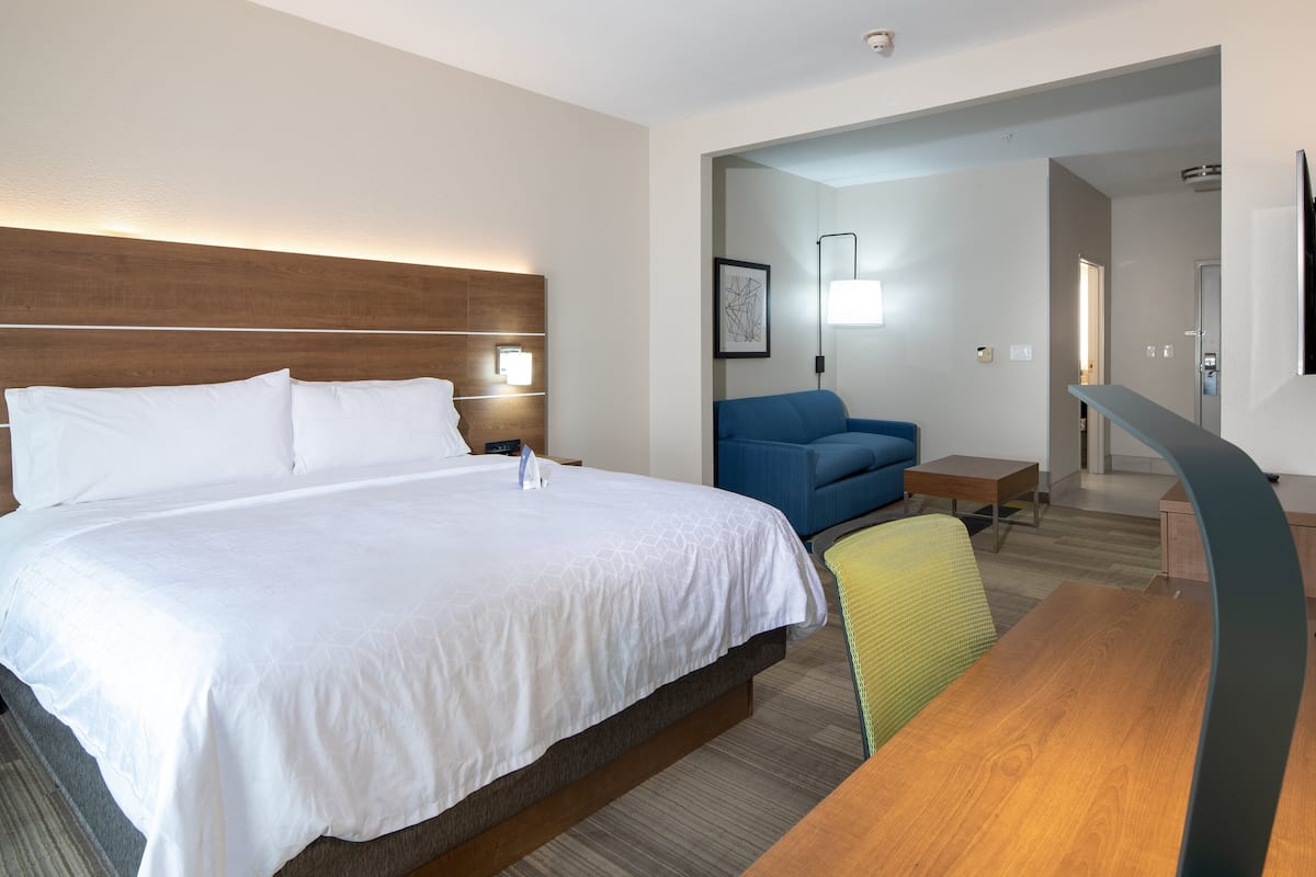 A hotel room with a large bed, a blue sofa, a wooden desk, and a TV.
