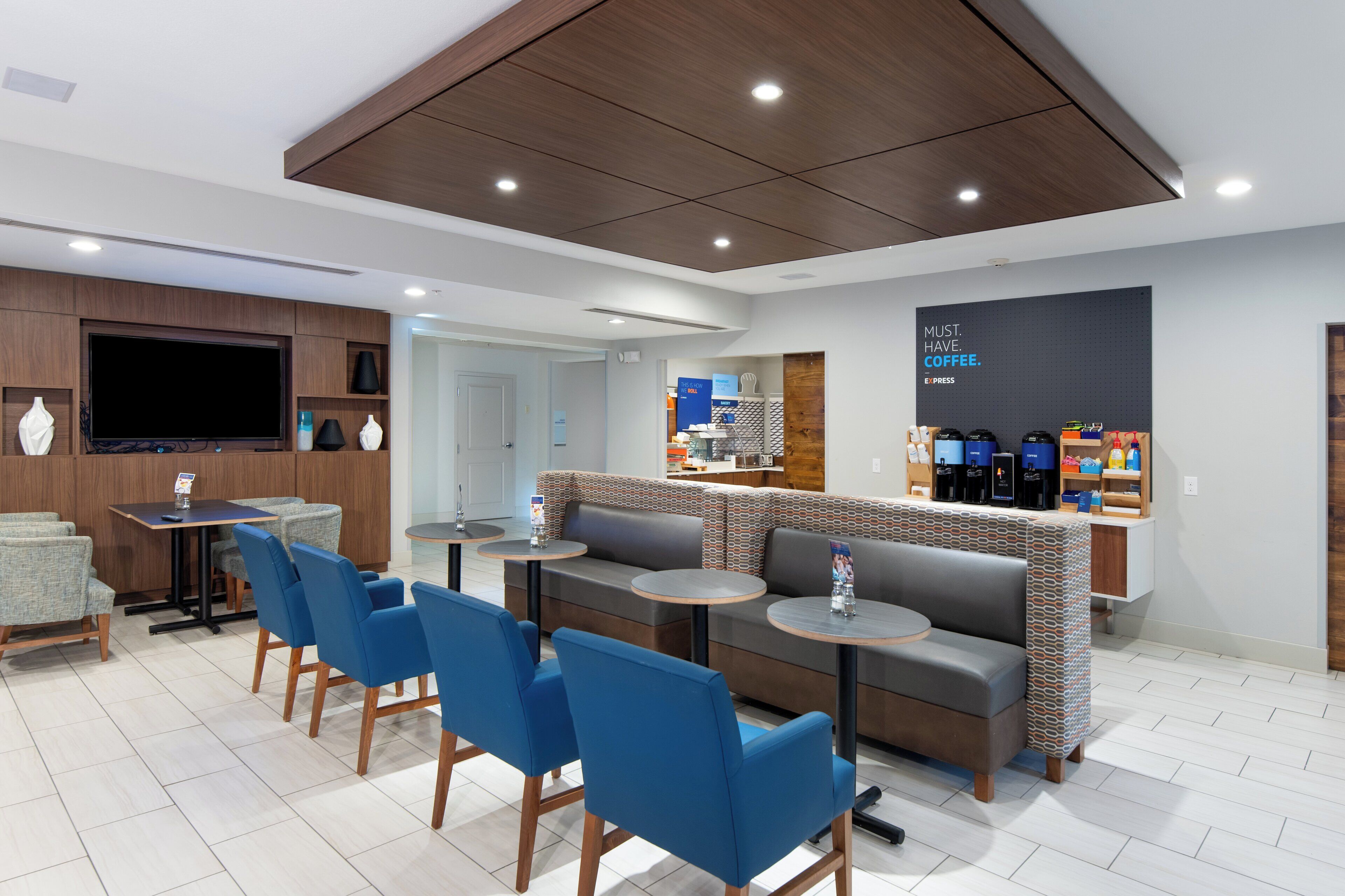 Un moderno vestíbulo de hotel con zonas de estar, una cafetería y un televisor.
