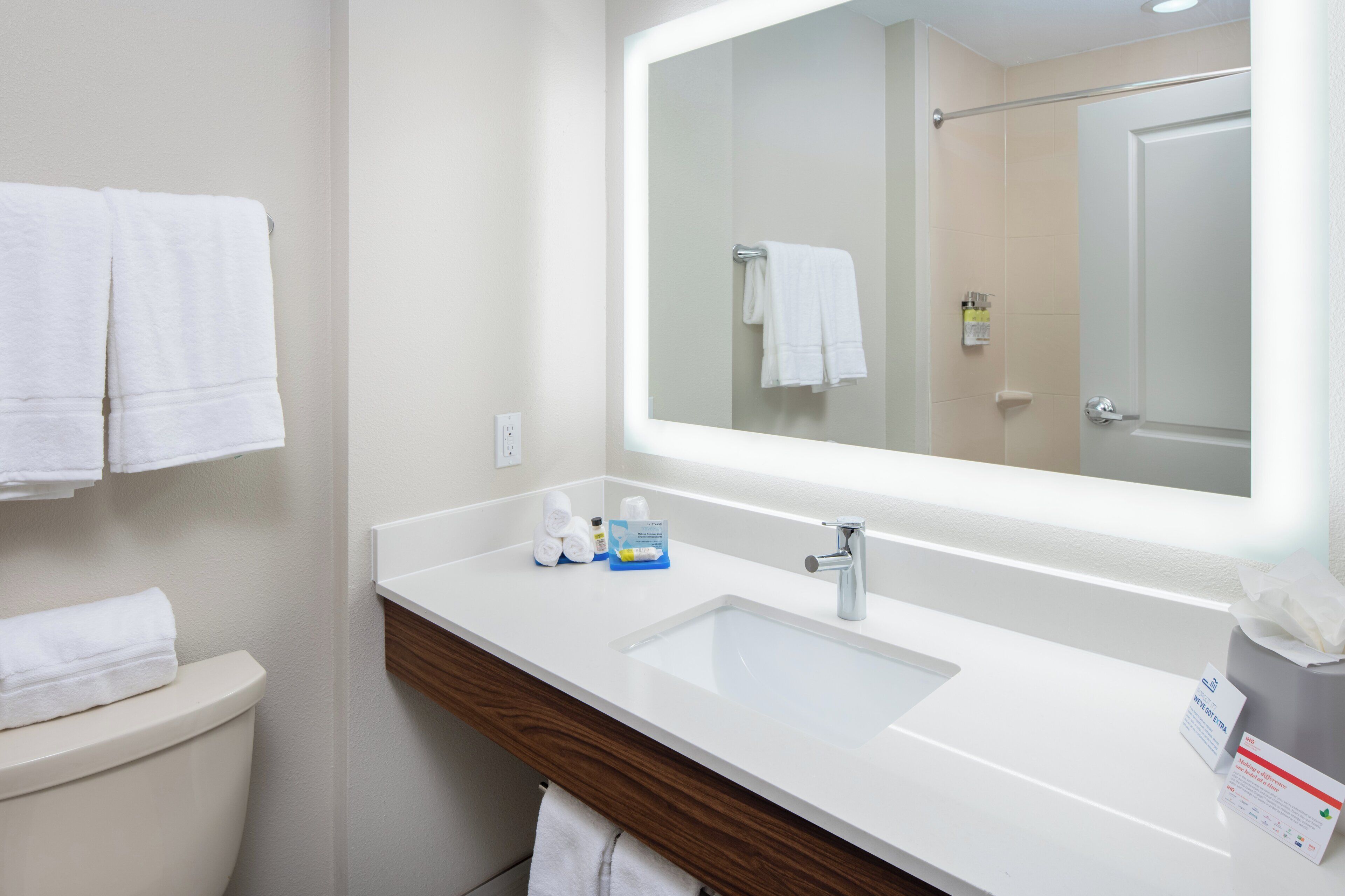 Un baño de hotel con un lavamanos blanco, un espejo y un inodoro.