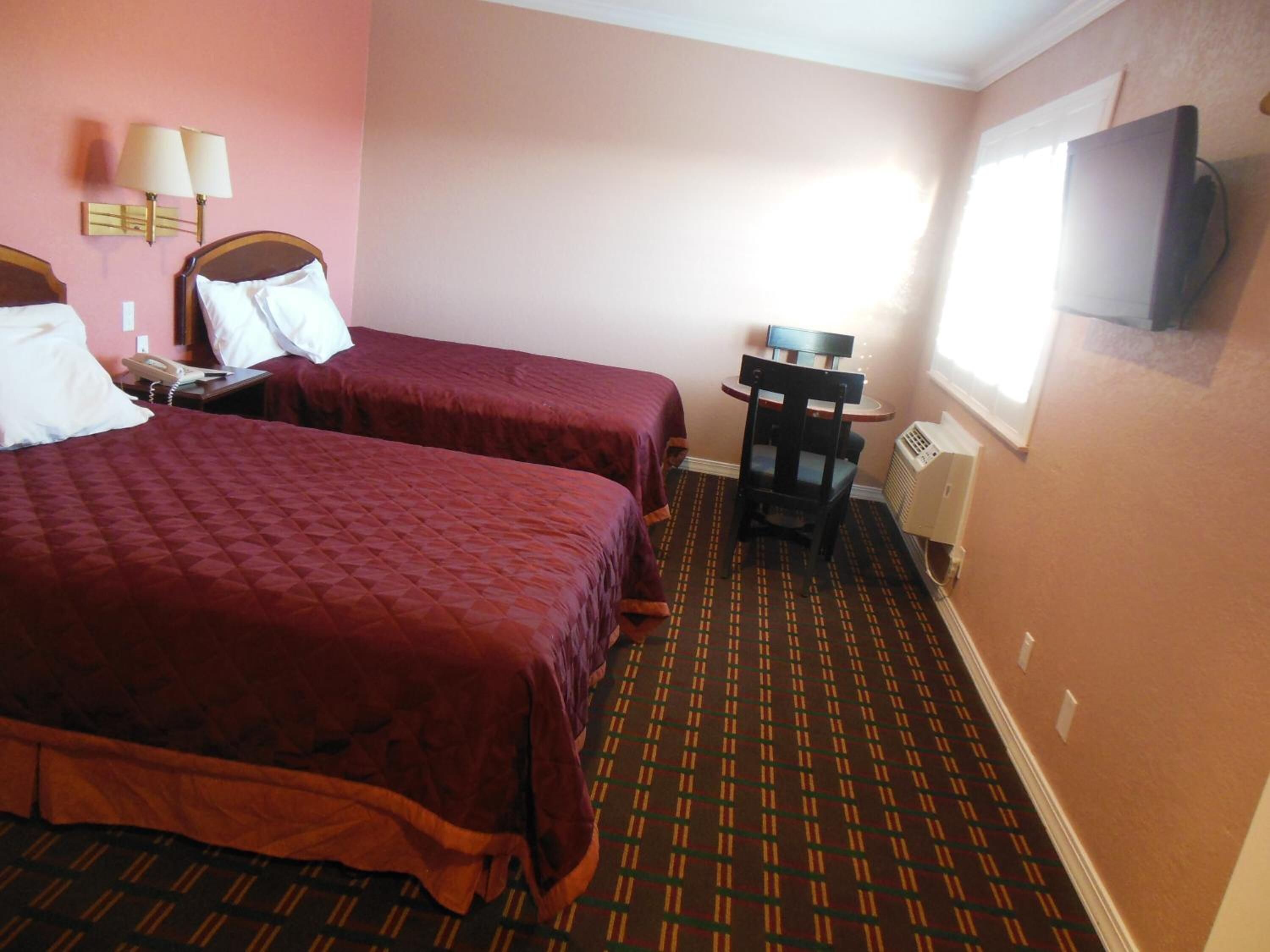 Une chambre d’hôtel avec deux lits, un bureau, une chaise, une télévision et une lampe fixée au mur.