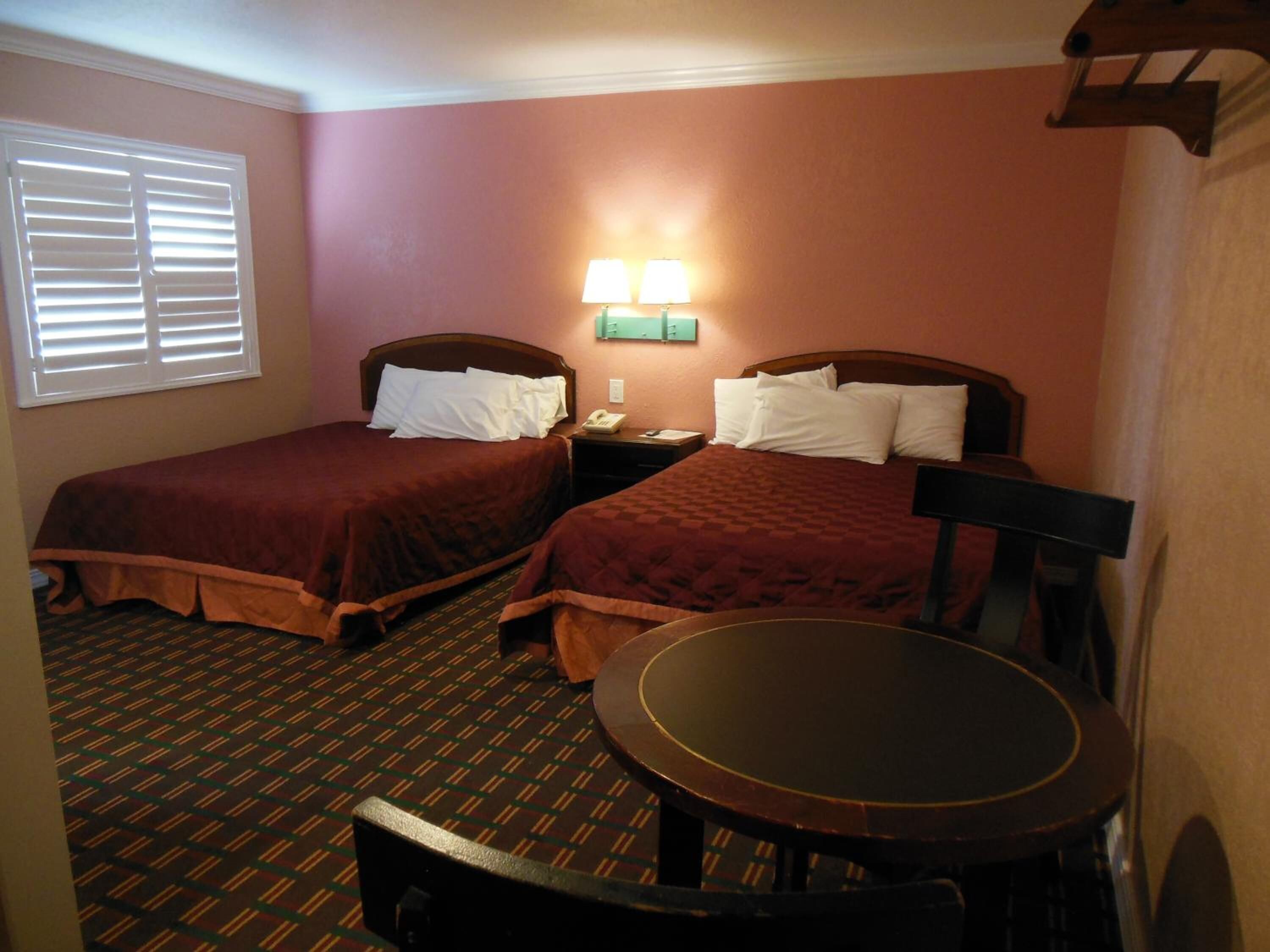 Een hotelkamer met twee bedden, een tafeltje en een raam met zonwering.
