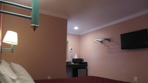 A hotel room with a bed, a bedside table with a lamp, a TV mounted on the wall, and a microwave on the table. - Sealamp Inn (Seaside)