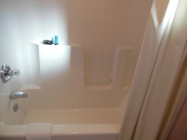 A standard white bathtub with a shower curtain, a glass shower door, and a small shelf with toiletries. - Sealamp Inn (Seaside)