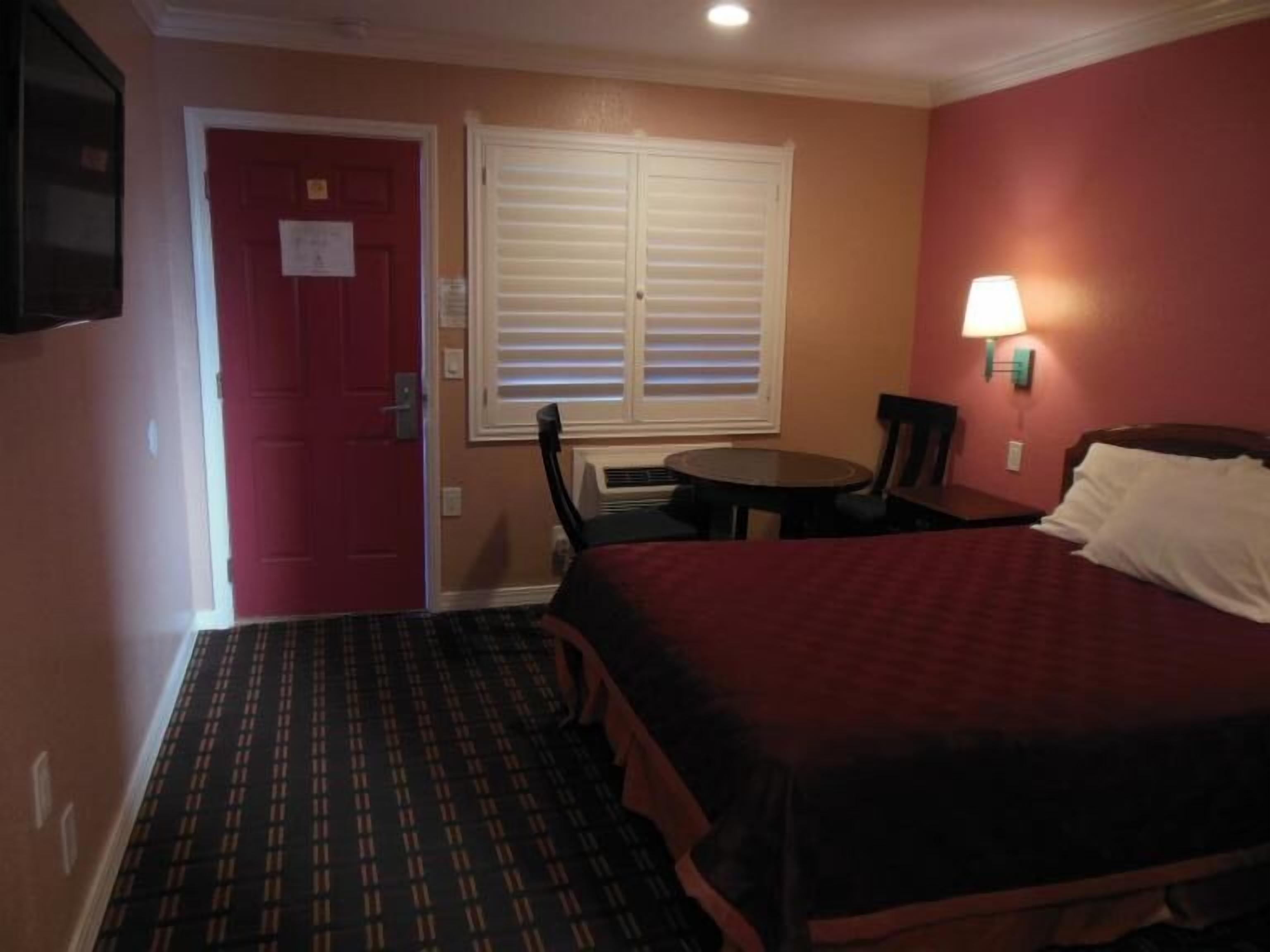 A hotel room with a bed, a table, a chair, a TV, and a window with blinds.
